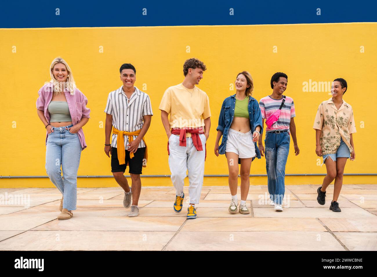 Multi-ethnische Gruppe junger Freunde, die Seite an seide vor der gelben Mauer laufen Stockfoto