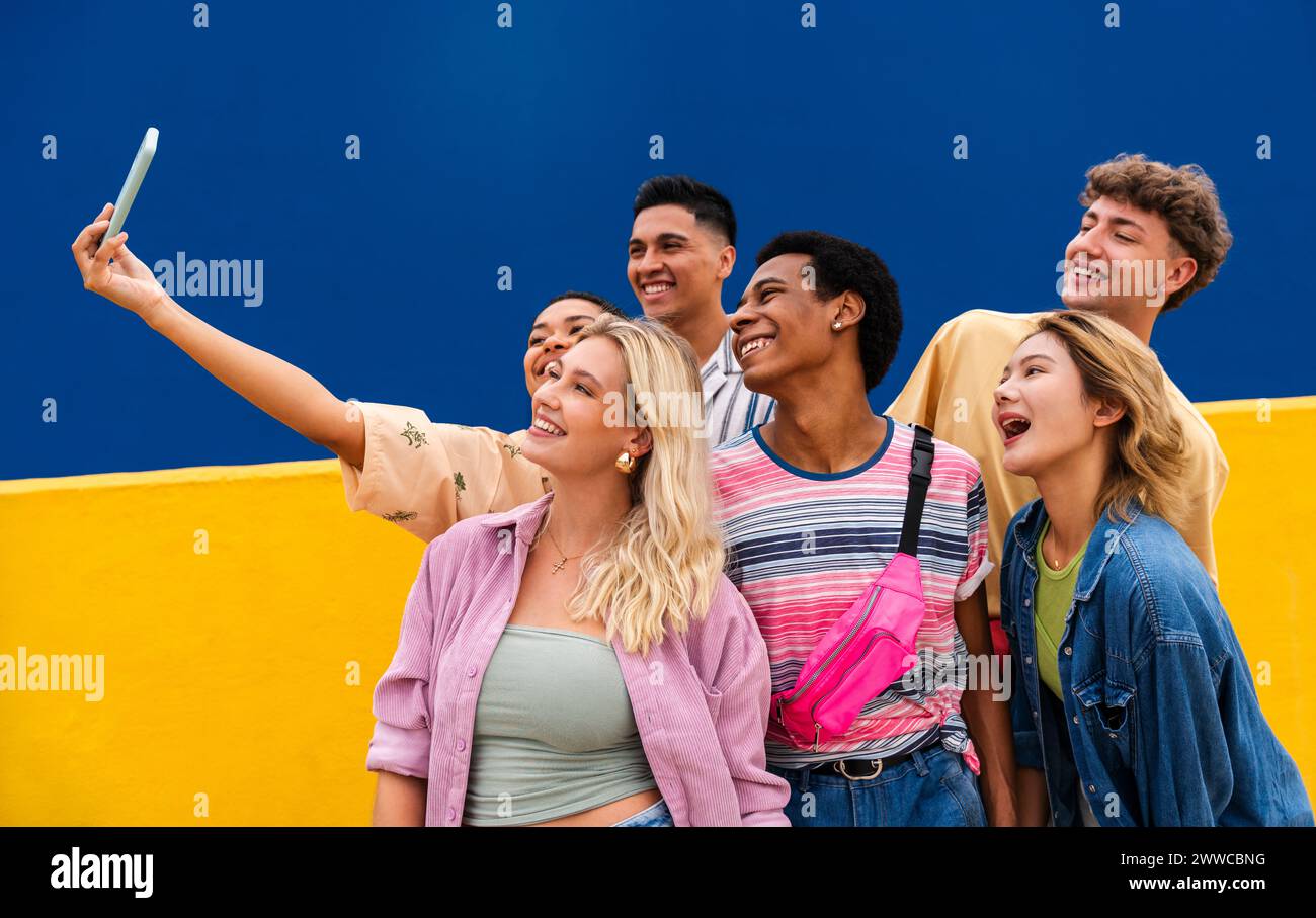 Lachende multiethnische Freunde machen Smartphone-Selfie vor der gelben Wand Stockfoto