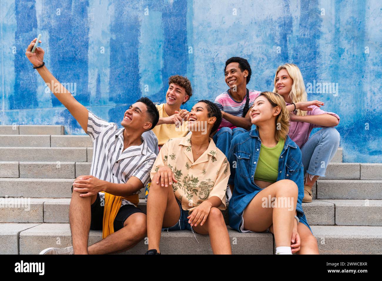 Glückliche Gruppe junger Leute, die Selfie auf Stufen vor der Wand machen Stockfoto