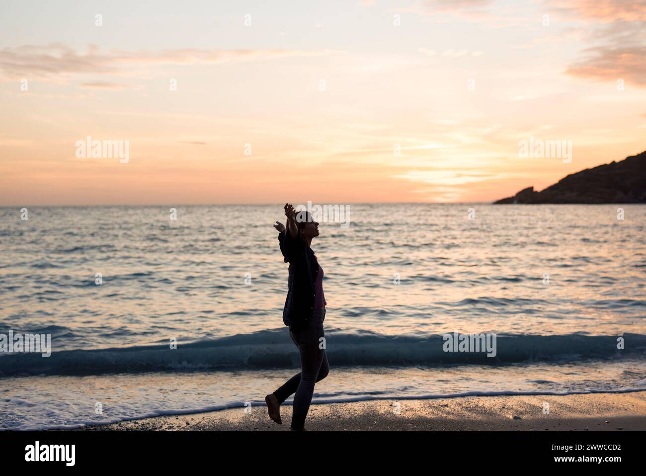 Sorglose Frau mit ausgestreckten Armen, die am Strand bei Sonnenuntergang läuft Stockfoto