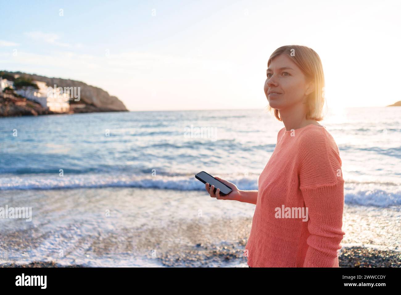 Nachdenkliche Frau mit Smartphone am Strand Stockfoto