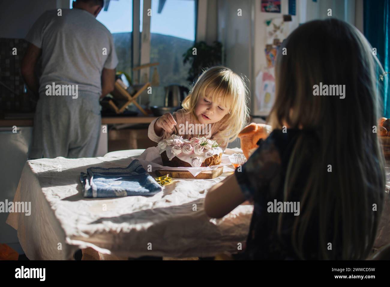 Mädchen isst Kuchen in der Nähe von Schwester in der Küche zu Hause Stockfoto