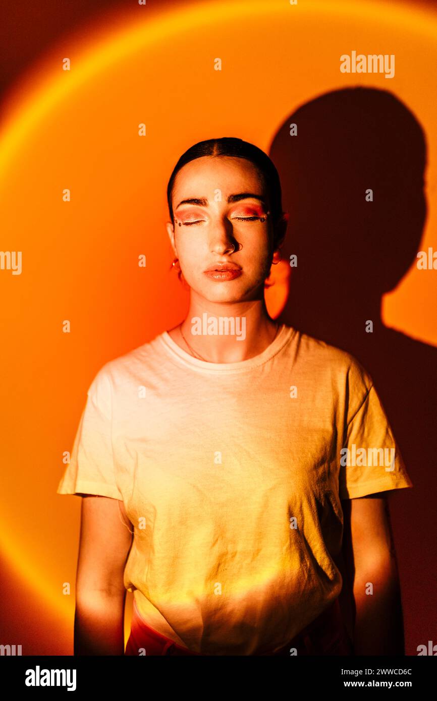 Junge Frau mit geschlossenen Augen in Neonlicht vor orangem Hintergrund Stockfoto