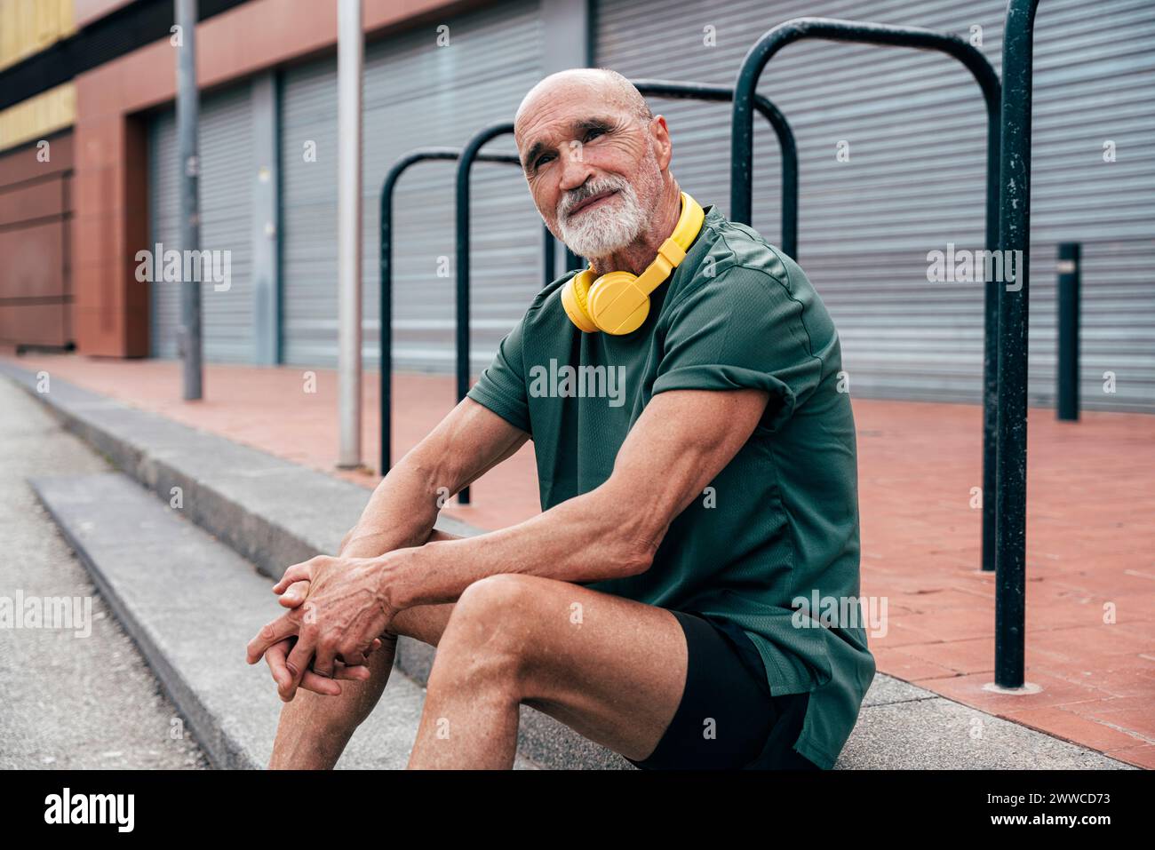Senior-Mann mit kabellosen Kopfhörern, der auf Stufen sitzt Stockfoto