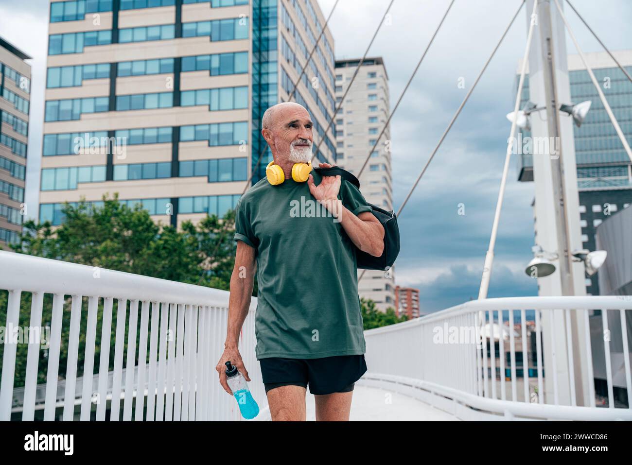 Aktiver Seniorenmann, der mit Energy Drink Flasche und Tasche auf der Fußgängerbrücke läuft Stockfoto