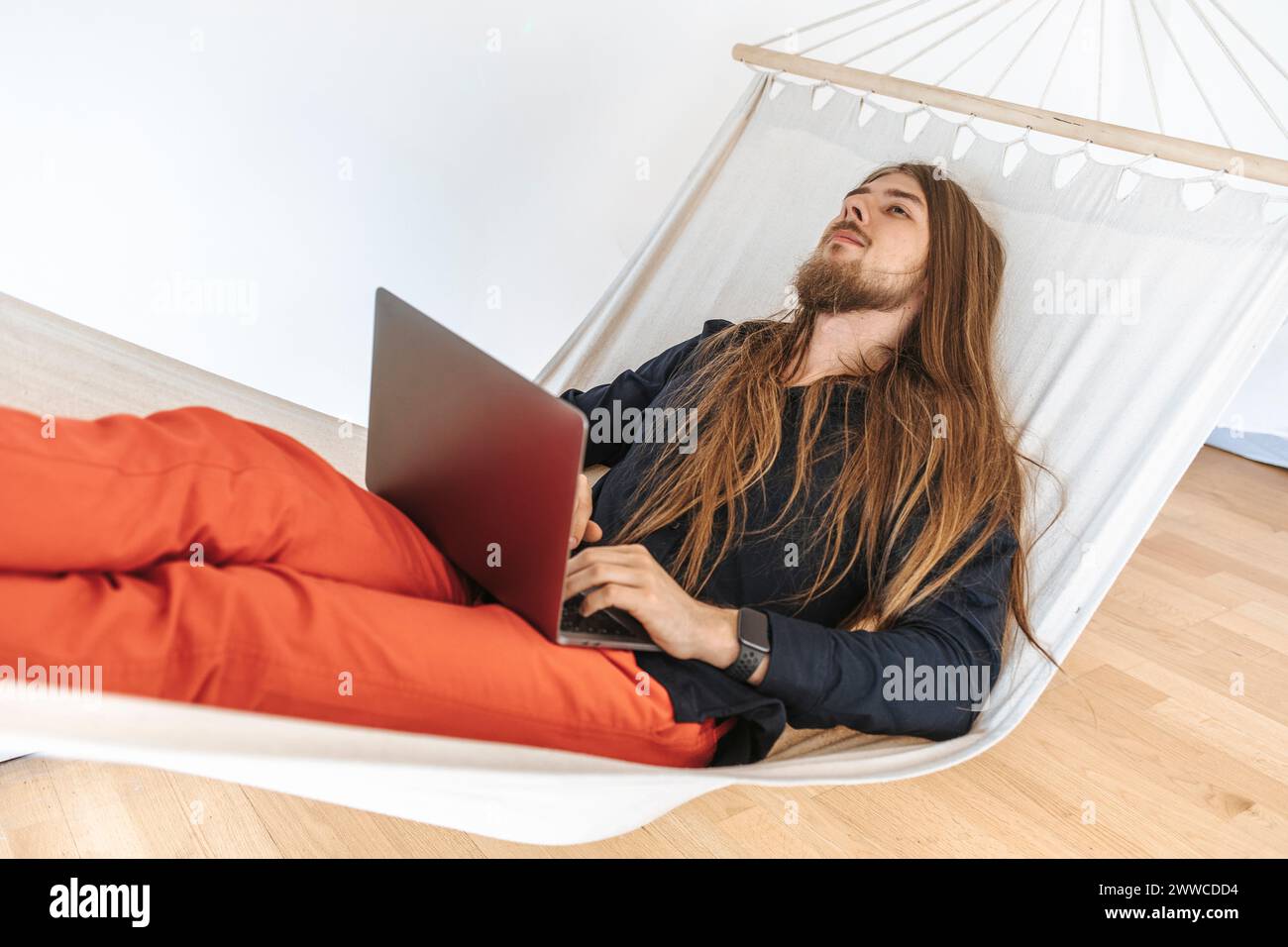 Junger Programmierer, der sich in der Hängematte mit Laptop beim Start im Büro entspannt Stockfoto