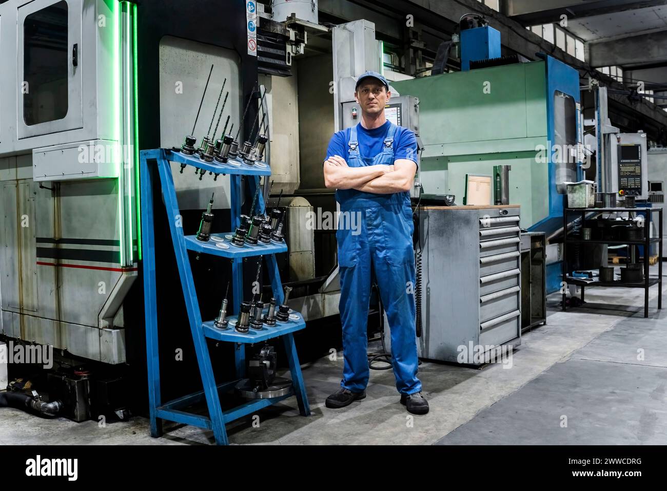 Selbstbewusster, ausgereifter Techniker, der mit den Armen von Maschinen in der modernen Industrie gekreuzt wird Stockfoto