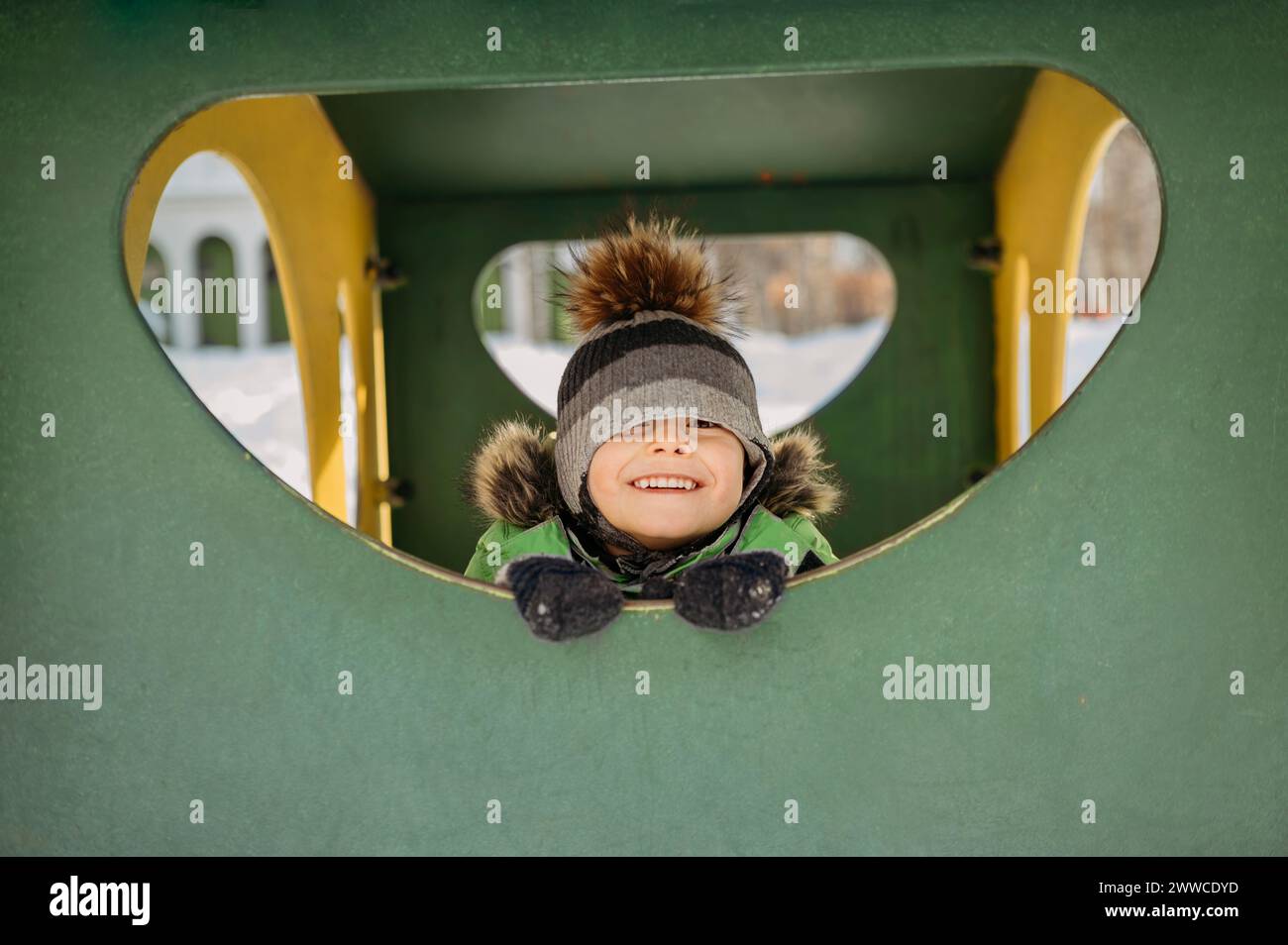 Lächelnder Junge in warmen Kleidern, der auf dem Spielplatz spielt Stockfoto