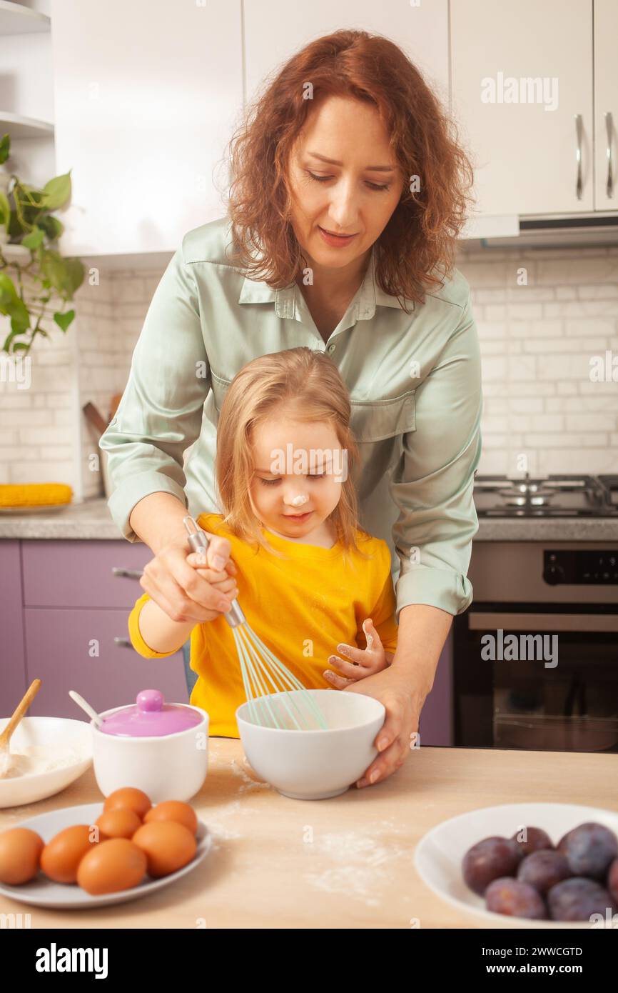Mutter und Tochter kochen Kuchen in lila Küche, Training und Entwicklung, interessantes Spiel und Hilfe. Glückliche Familie zusammen. Stockfoto
