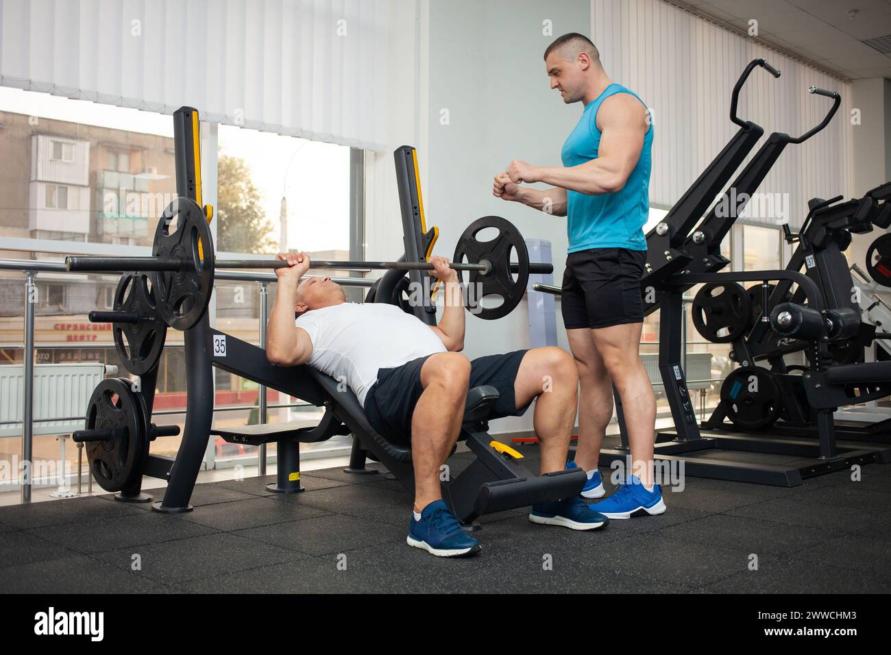 Der Trainer bringt dem Mann die richtige Technik bei, um die Übung am Simulator im Fitnessstudio durchzuführen. Gewichtsverlust, Muskelaufbau, gesunde lifestyl Stockfoto