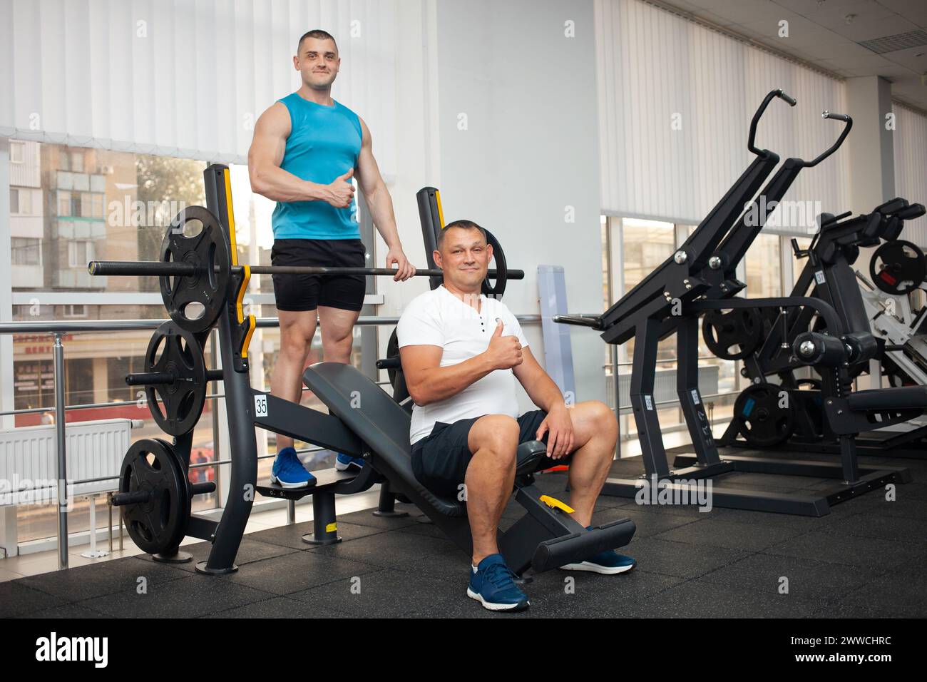 Der Trainer bringt dem Mann die richtige Technik bei, die Übung am Simulator im Fitnessstudio durchzuführen. Gewichtsverlust, Muskelaufbau, gesunder Lebensstil, A Stockfoto