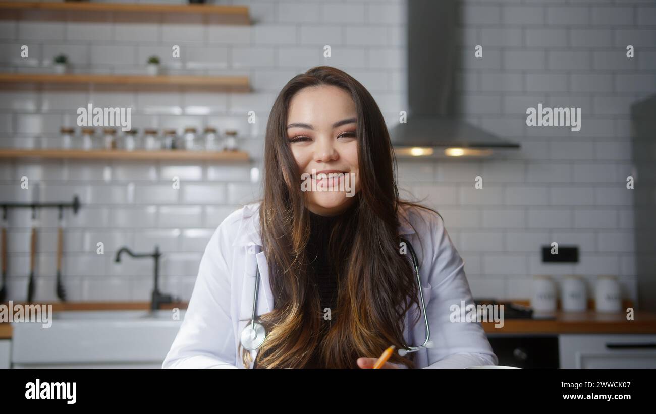 Professionelle asiatische Ärztin trägt weiße Uniform mit Stethoskop, die Videokonferenzen führt, online mit dem Patienten chatten, die Kamera in die Webca schaut Stockfoto
