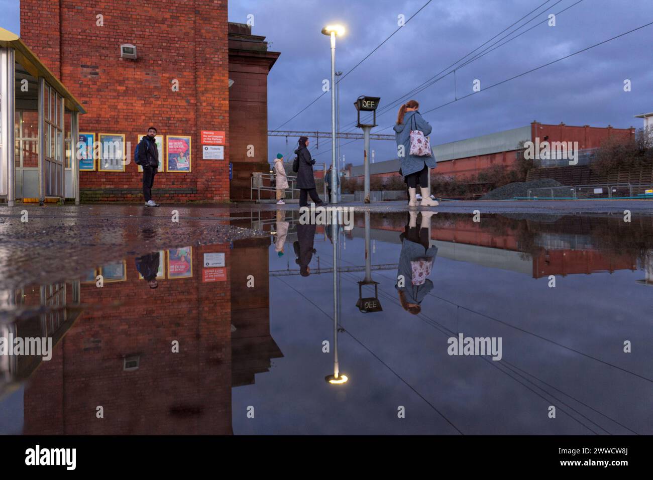 Bahnhof Edge Hill, Passagiere, die auf einen Zug der Northern Rail warten, spiegeln sich in einer Pfütze auf dem Bahnsteig Stockfoto