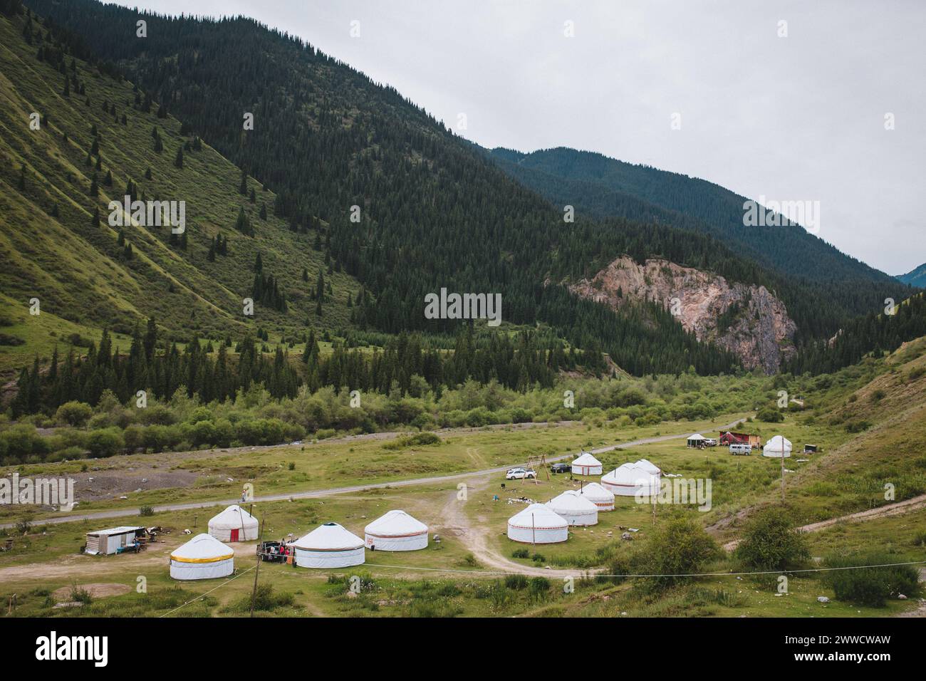 Kirgisisches Jurtenlager in den Bergen Zentralasiens. Nomadisches Dorf im Tal in der Nähe des Flusses unter bewölktem Himmel. Stockfoto