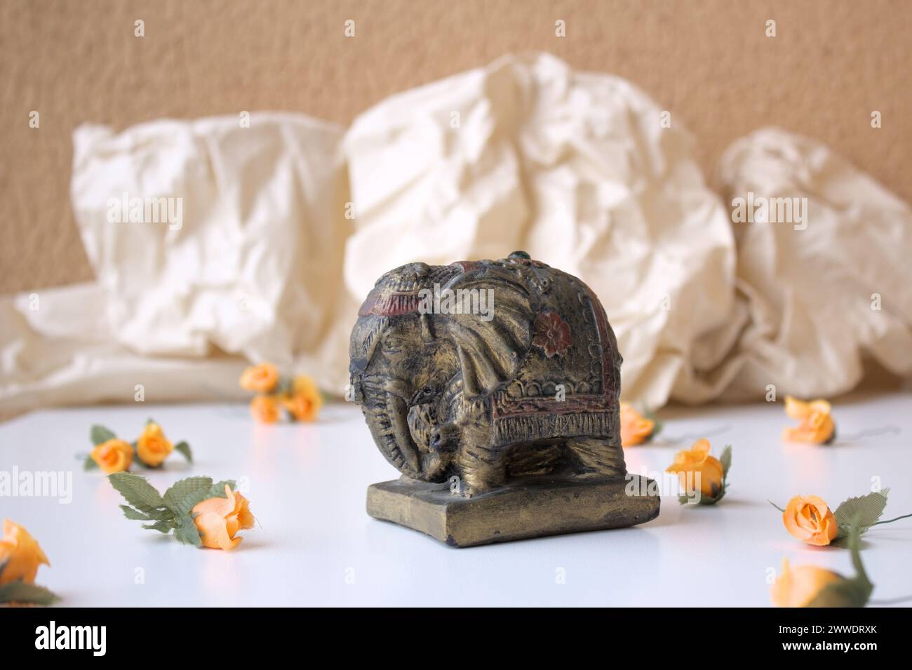 Alte indische Elefantenstatue für Wohnkultur auf weißem Tisch mit orangefarbenen Blumen. Stockfoto
