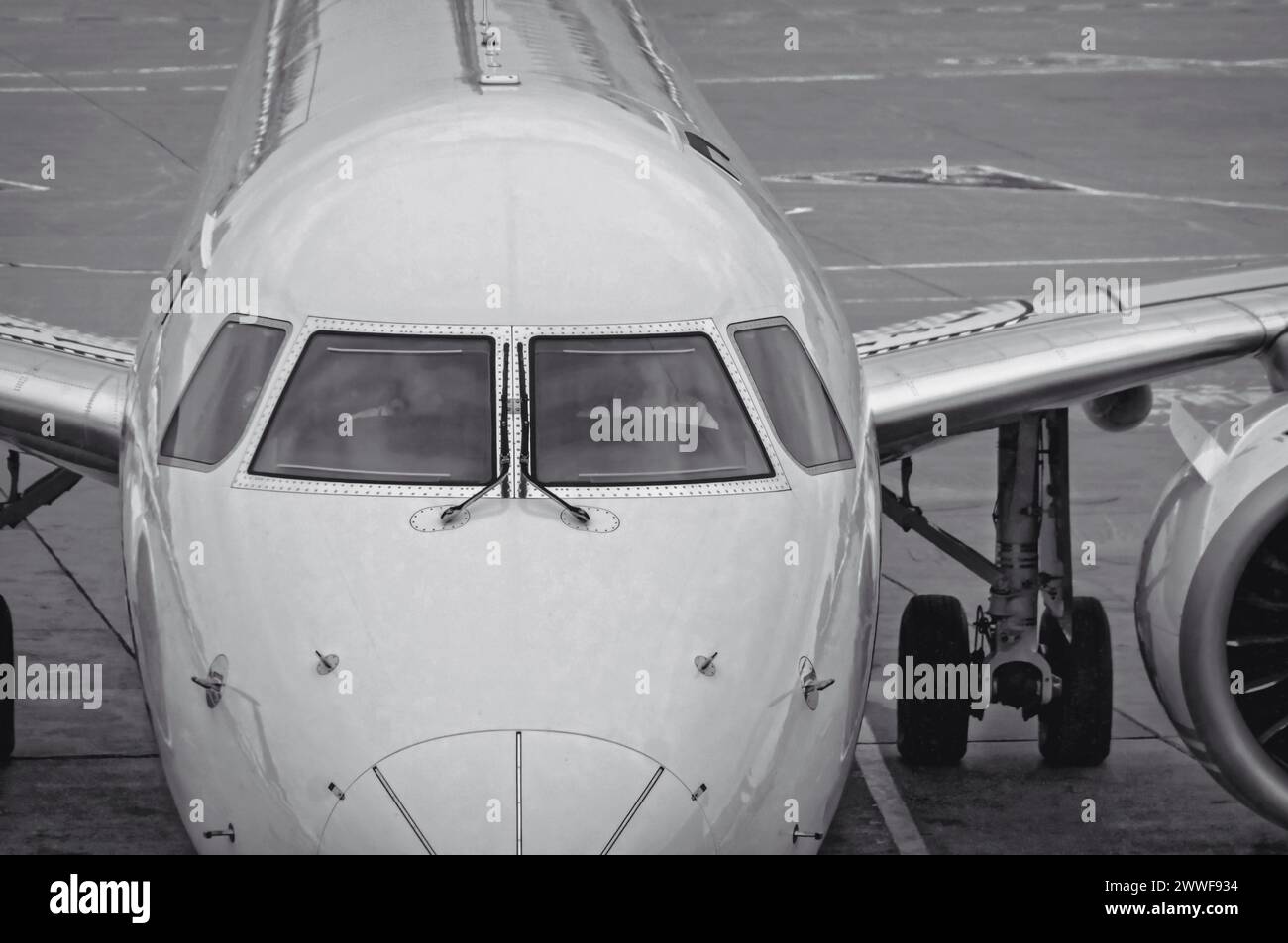 Vorderansicht des weißen modernen Düsenflugzeugs mit Nahaufnahme der Cockpitfenster. Das Flugzeug sitzt auf einem Betonbelag mit lackierten Fahrspurlinien. Schwarz und Stockfoto