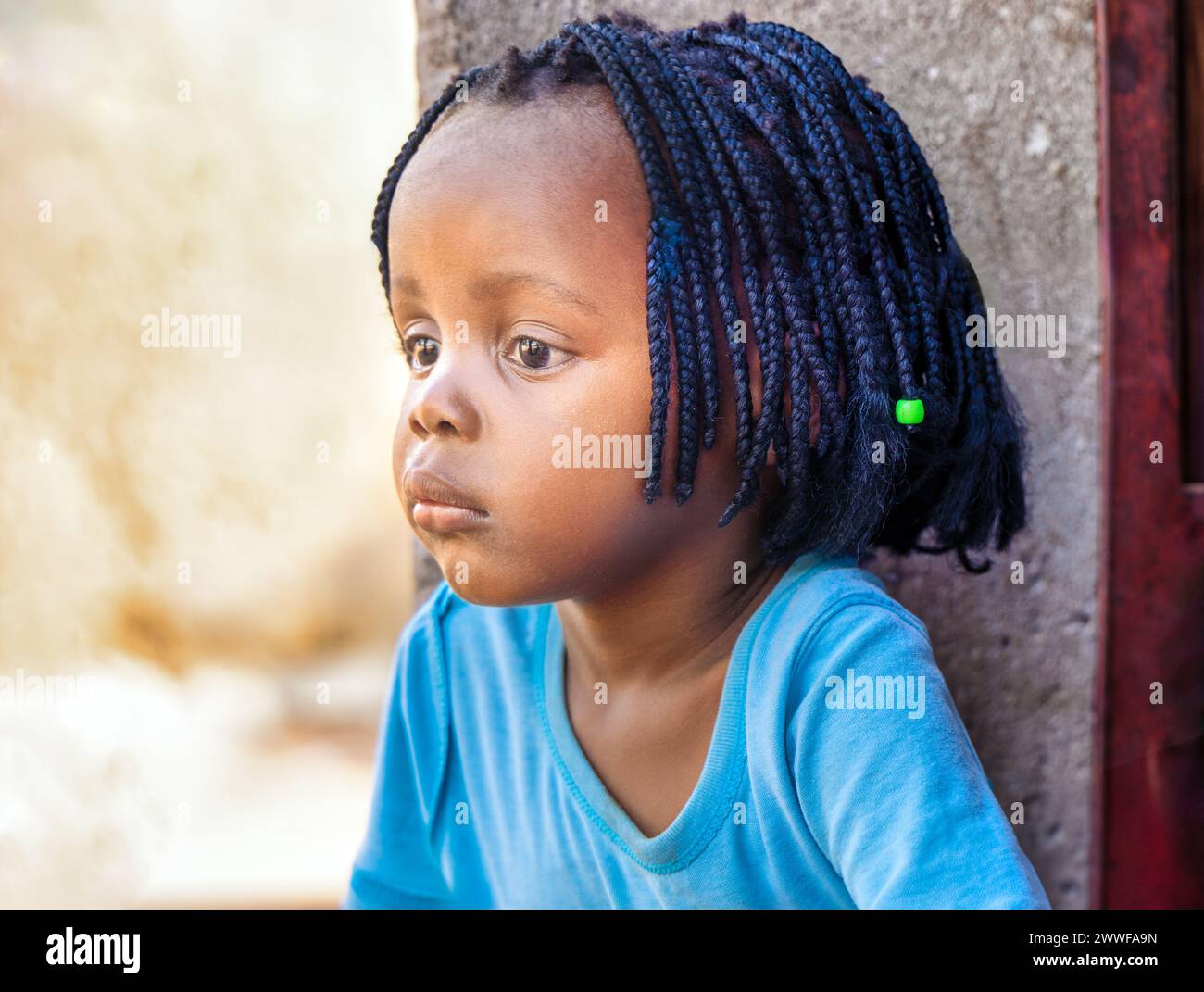 afrikanisches Dorfmädchen mit Zöpfen vor ihrem Haus, auf der Veranda Stockfoto