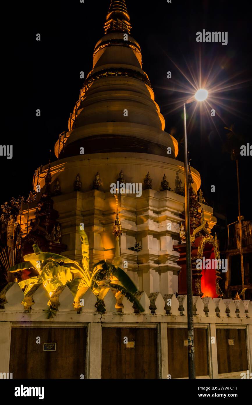 Die warmen Töne eines Tempels werden durch ein Scheinwerferlicht am Nachthimmel in Chiang Mai, Thailand, hervorgehoben Stockfoto