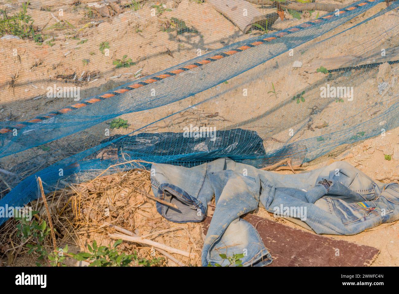 Verlassene Kleidung und Baunetz auf trockenem Boden, das Abfall und Fahrlässigkeit darstellt, in Südkorea Stockfoto