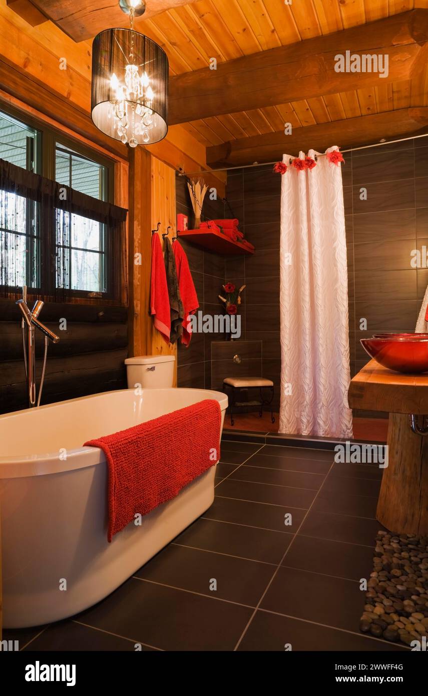 Weiße freistehende Badewanne, Duschkabine und rote Waschbecken im Hauptbadezimmer im modernen Blockhaus, Quebec, Kanada Stockfoto