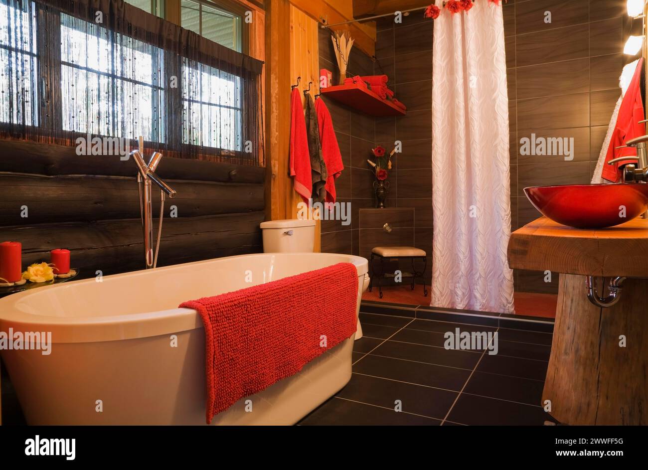 Weiße freistehende Badewanne, Duschkabine und rote Waschbecken im Hauptbadezimmer im modernen Blockhaus, Quebec, Kanada Stockfoto