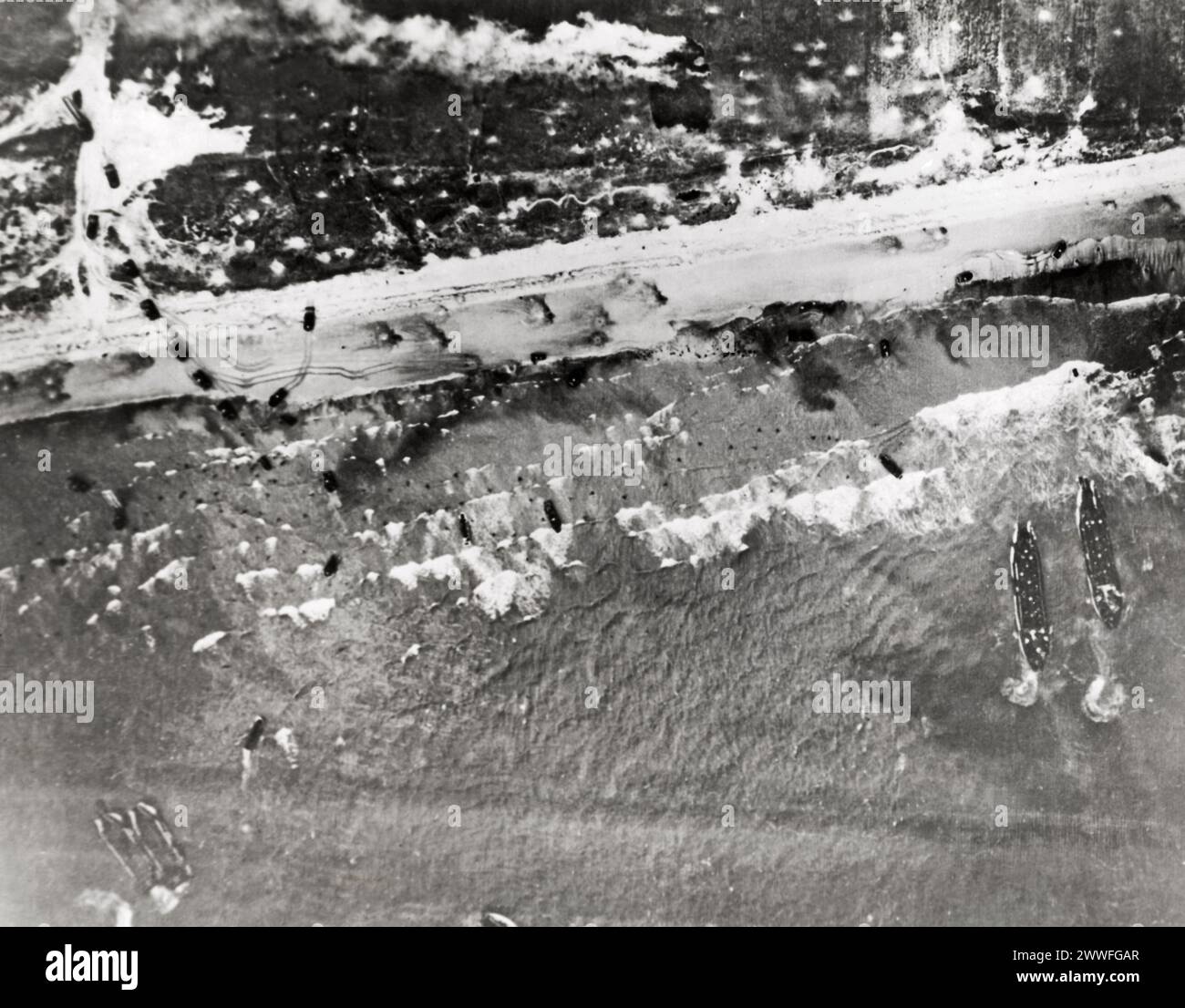 Normandie, Frankreich, 10. Juni 1944, Sturmboote belauschen ihre Fracht mit Soldaten an den Invasionsstränden der Normandie in Frankreich. Kleine Flecken, die im Wasser mit weißem Deckel zu sehen sind, sind Truppen, die auf das Ufer waten. Tanks und andere Kraftfahrzeuge haben bereits mit der Fahrt ins Landesinnere begonnen. Größere Schiffe warten vor der Küste, während der Kampf um die Befreiung Europas planmäßig voranschreitet. Stockfoto