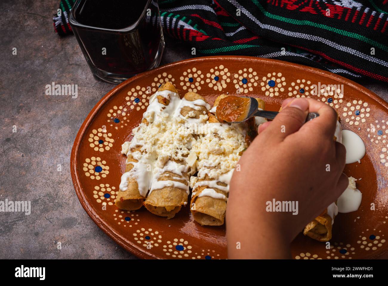 Frau löffelt Salsa auf einem Teller mit goldenen Kartoffeltacos. Mexikanisches Essen. Stockfoto