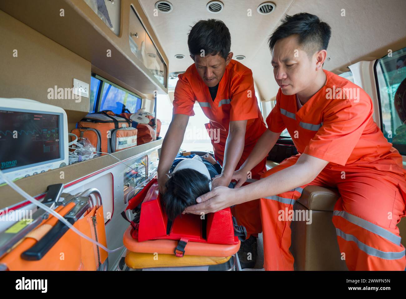 Zwei Sanitäter in orangefarbenen Uniformen helfen einem Patienten in einem Krankenwagen. Stockfoto