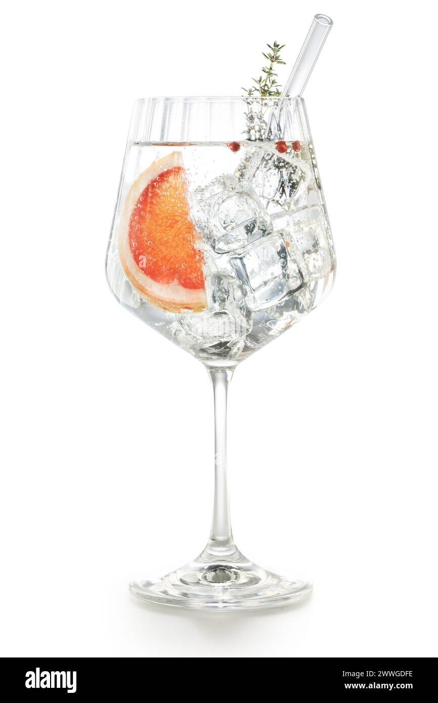 Gekräuseltes Ballonglas aus Gin Tonic mit Grapefruit, rosa Pfeffer, Thymianstab und Trinkstroh aus Glas isoliert auf weißem Hintergrund. Stockfoto