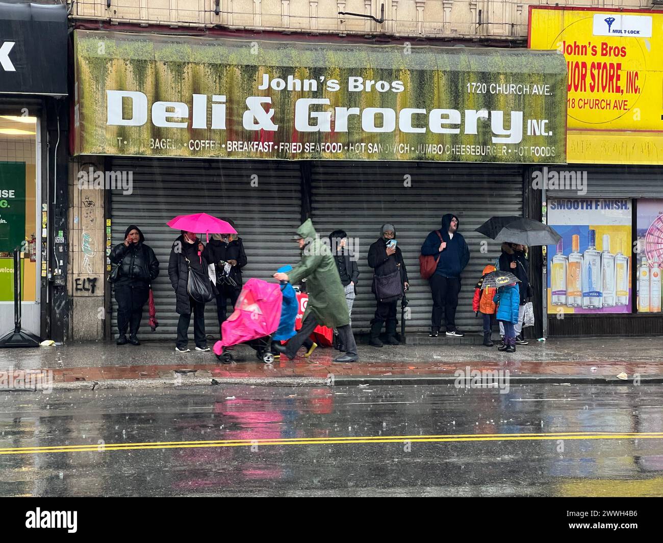 Die Leute warten an einem regnerischen Tag entlang der Church Avcenue im Stadtteil Flatbush in Brooklyn, New York, auf einen Bus. Stockfoto