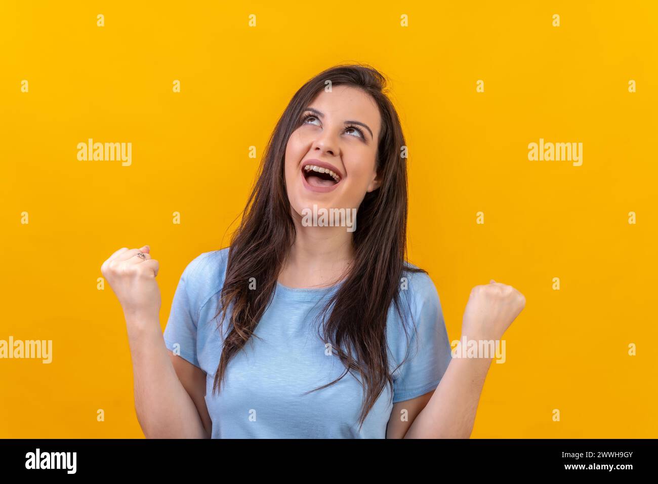 Studio-Porträt mit gelbem Hintergrund einer Frau, die aufblickt und feiert Stockfoto