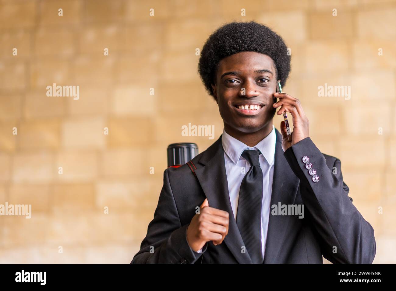 Frontales Nahaufnahme-Porträt mit Kopierraum eines jungen glücklichen Architekten mit Afro-Frisur und Anzug, der draußen telefoniert Stockfoto