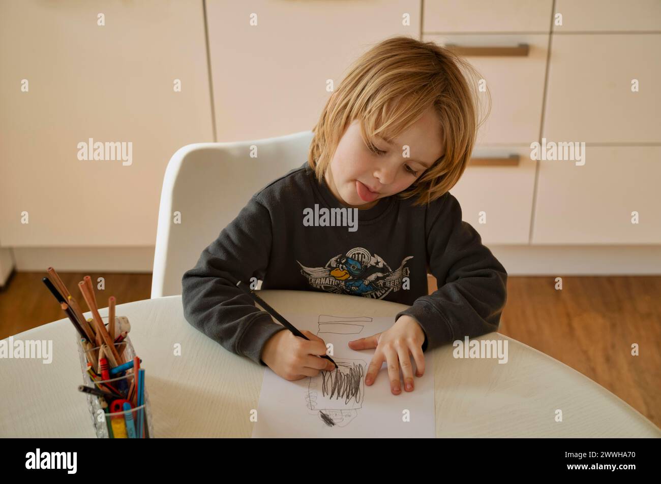 Innenfoto, Junge, 4-5 Jahre, blond, zeichnen auf Blatt Papier, Bleistifte, Tisch, strapazieren, mit der Zunge spielen, Stuttgart, Baden-Württemberg, Deutschland Stockfoto