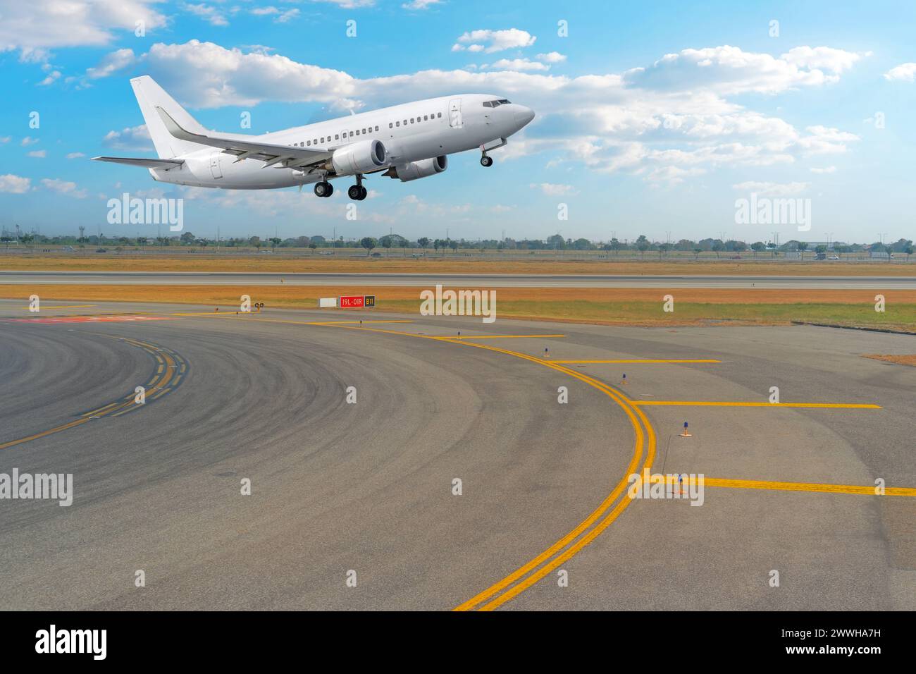 Blick auf die Kurve vom Rollweg auf die Start- und Landebahn und ein Passagierflugzeug, das vor dem Hintergrund abhebt. Stockfoto