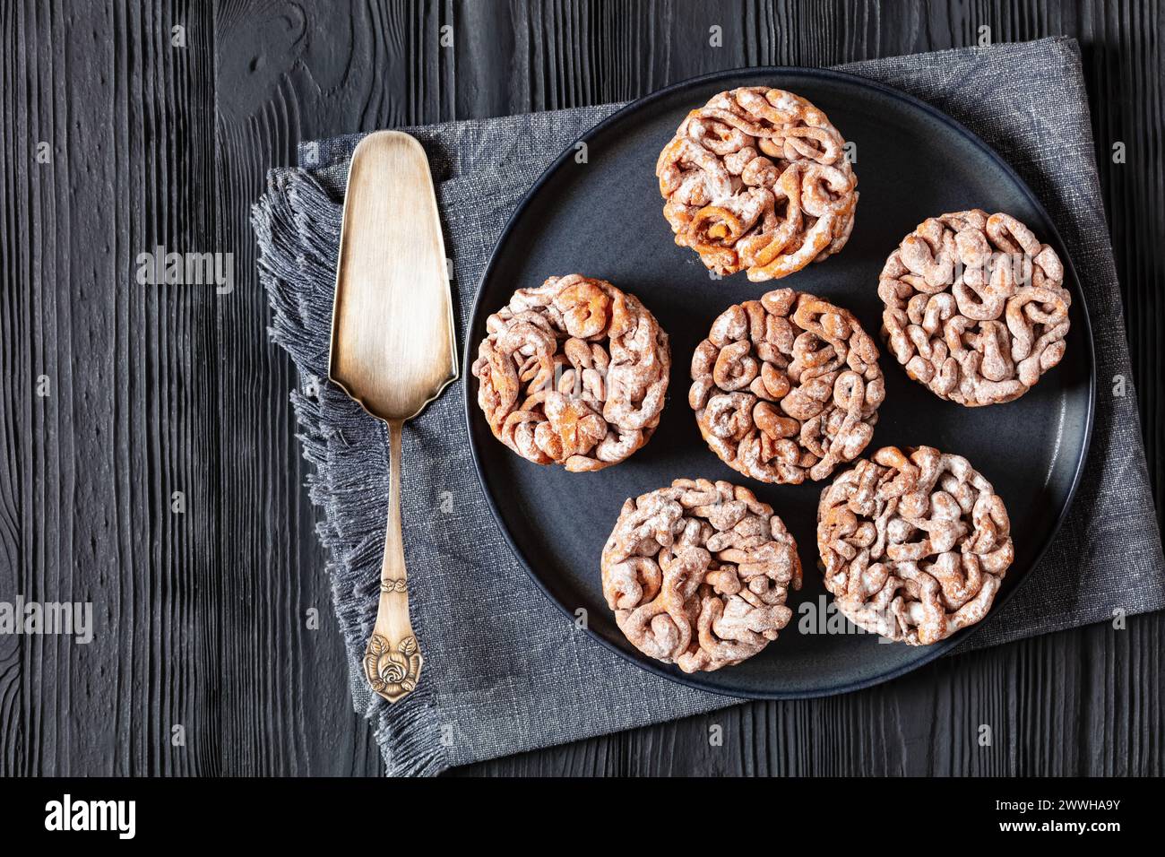 Tippaleipa, finnischer Mai Tag Trichterkuchen frittiert und mit Puderzucker bestäubt für einen süßen Teller auf schwarzem Holztisch mit Kuchenschaufel, Horizo Stockfoto
