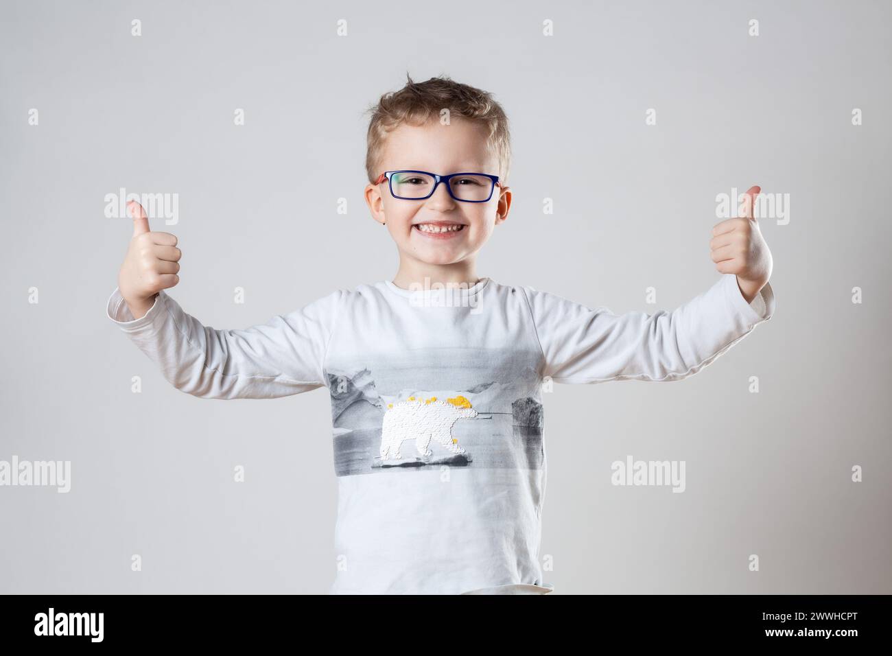 Ein kleiner Junge, der eine Brille trägt, gibt enthusiastisch die Daumen hoch Stockfoto