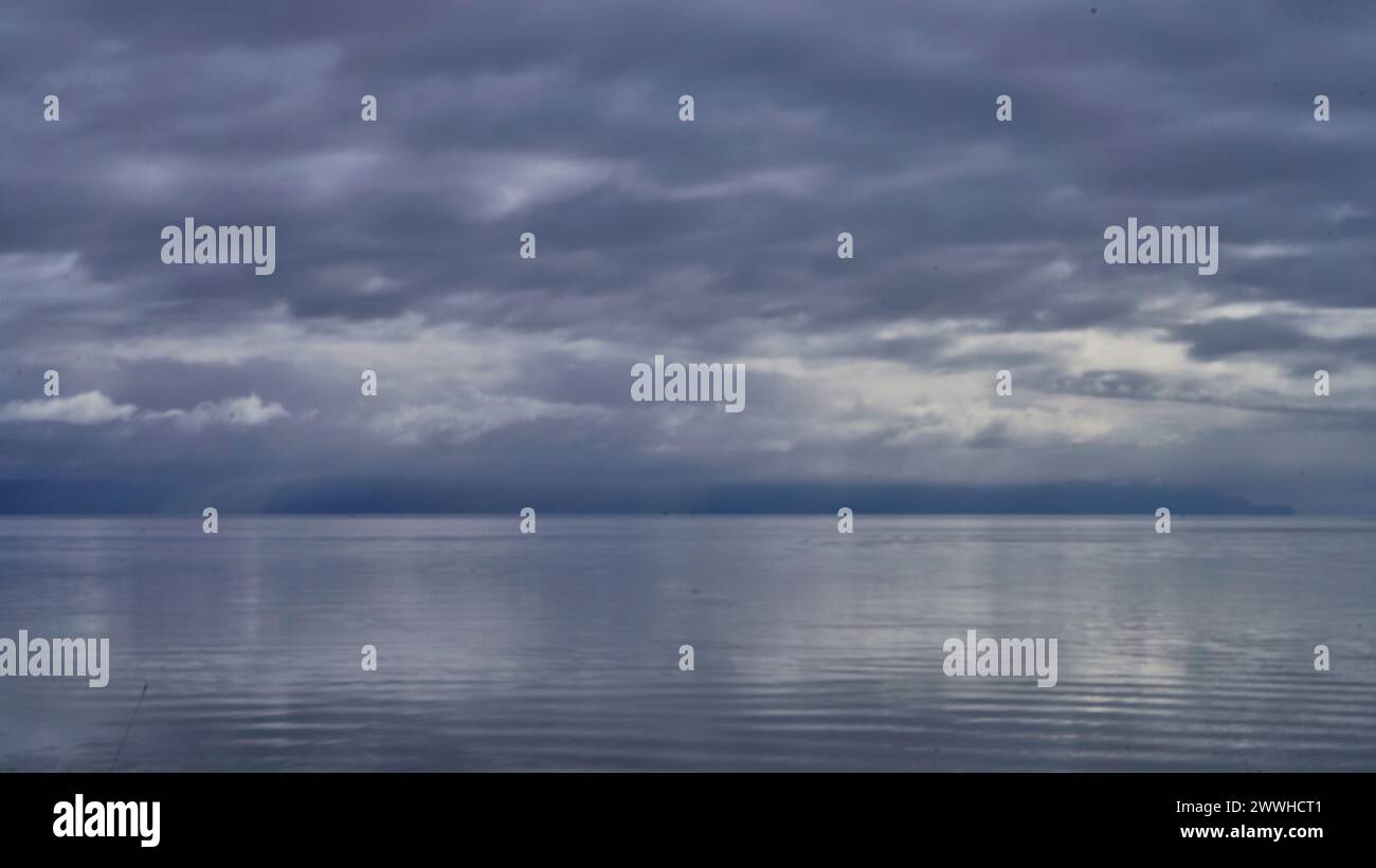 Minimalistischer Blick auf das ruhige graublaue Meer eines sich nähernden Regensturms mit Wolkenreflexionen. Stockfoto