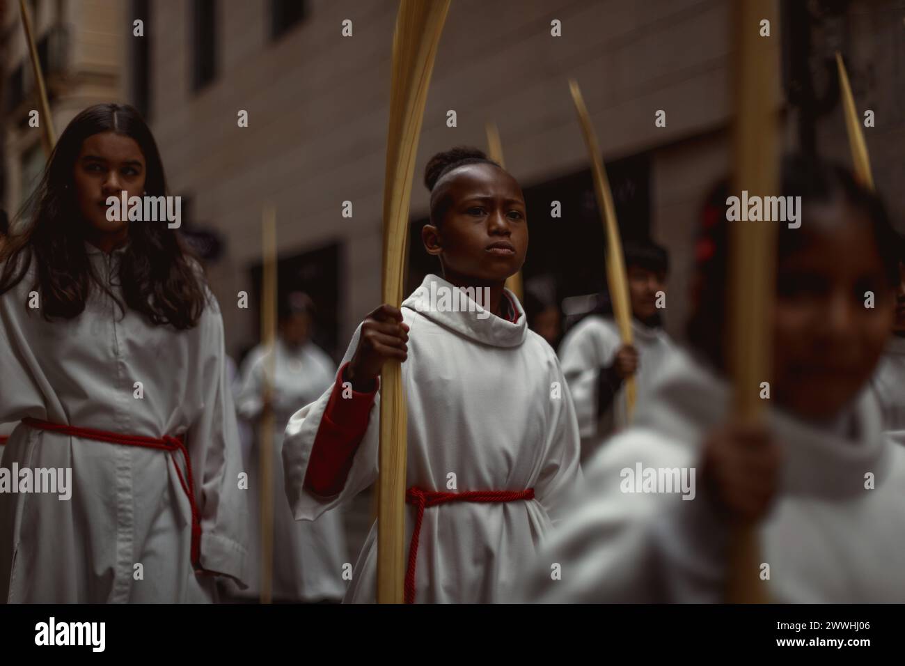 Barcelona, Spanien. März 2024. Junge Pönitenten aus der 'Gran Poder und Macarena Esperanza'-Bruderschaft gehen während der Palmensonntagsprozession in Barcelona mit Palmenzweig durch die Straße. Credit: Matthias Oesterle/Alamy Live News Stockfoto