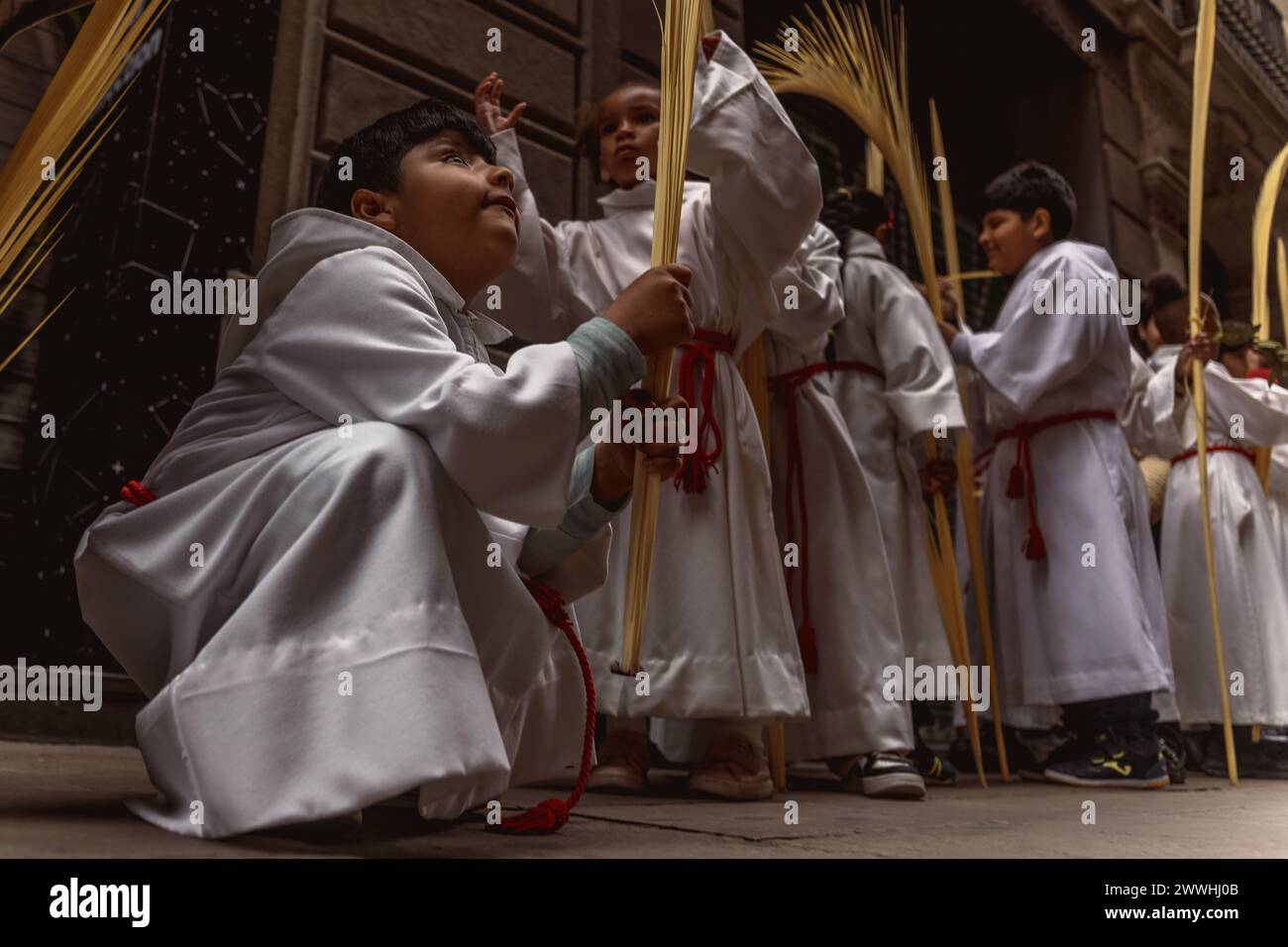 Barcelona, Spanien. März 2024. Junge Pönitenten aus der 'Gran Poder und Macarena Esperanza'-Bruderschaft gehen während der Palmensonntagsprozession in Barcelona mit Palmenzweig durch die Straße. Credit: Matthias Oesterle/Alamy Live News Stockfoto