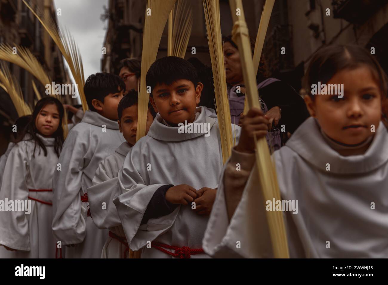 Barcelona, Spanien. März 2024. Junge Pönitenten aus der 'Gran Poder und Macarena Esperanza'-Bruderschaft gehen während der Palmensonntagsprozession in Barcelona mit Palmenzweig durch die Straße. Credit: Matthias Oesterle/Alamy Live News Stockfoto