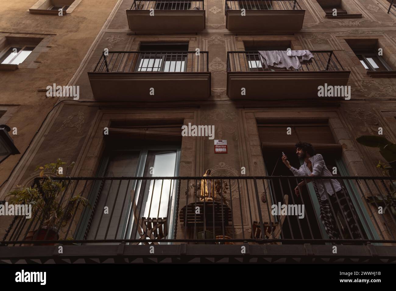 Barcelona, Spanien. März 2024. Ein Nachbar hat eine religiöse Figur auf den Tisch seines Balkons gestellt, um ein Foto von der Palmensonntagsprozession in Barcelona zu machen Credit: Matthias Oesterle/Alamy Live News Stockfoto