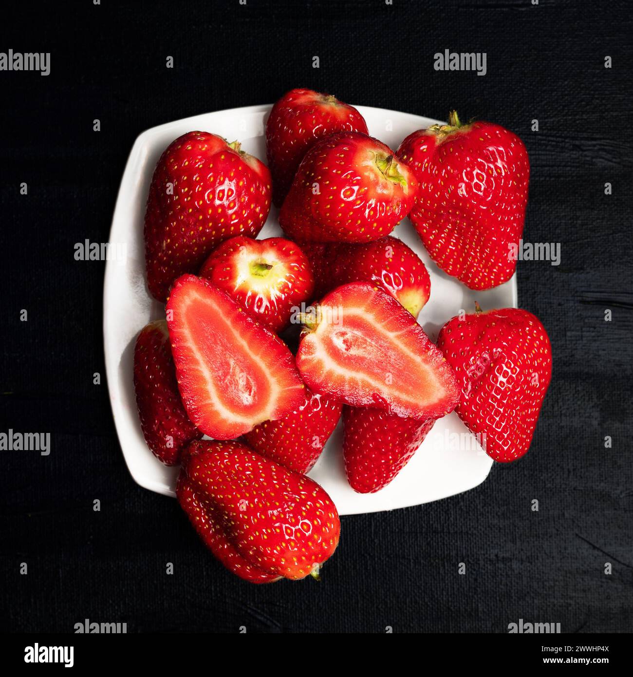 Erdbeeren auf einem weißen Teller vor schwarzem Hintergrund. Rote Früchte. Gesunde Ernährung. Vegane Ernährung. Moody Foto von Früchten Stockfoto