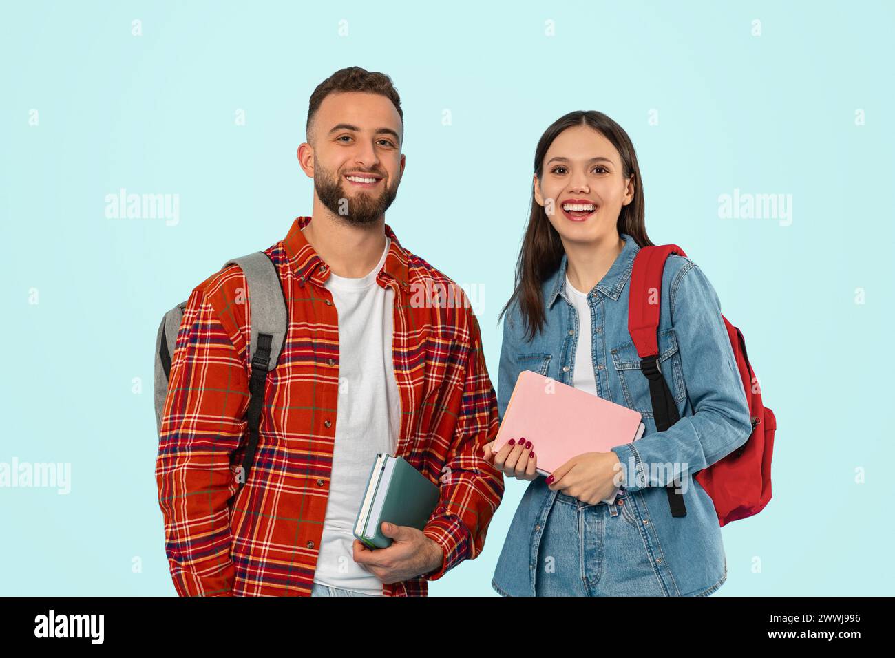 Fröhliches Paar posiert lässig mit Rucksäcken und Lehrbüchern im Studio Stockfoto