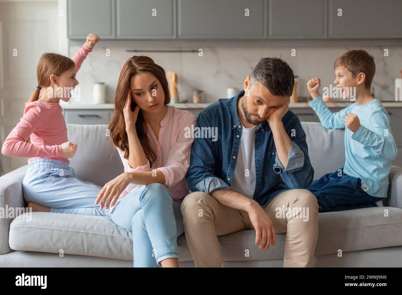 Zwei Kinder, die sich anschreien, gestresste Eltern, die neben ihnen sitzen Stockfoto