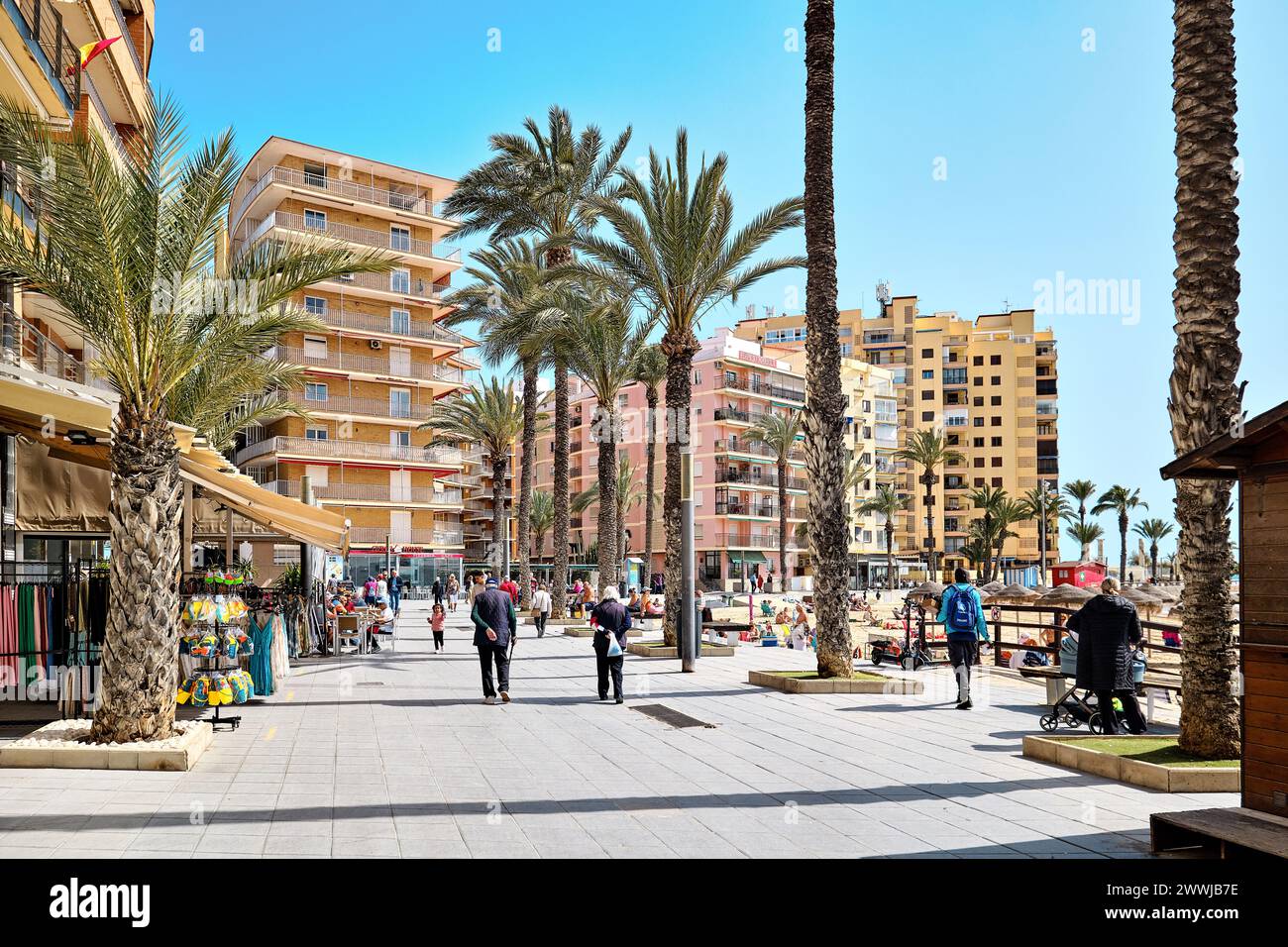 Torrevieja, Spanien-14. März 2024: Touristen schlendern entlang der Uferpromenade mit Palmen gesäumten Straße mit Café und Restaurants im Frühling Stockfoto
