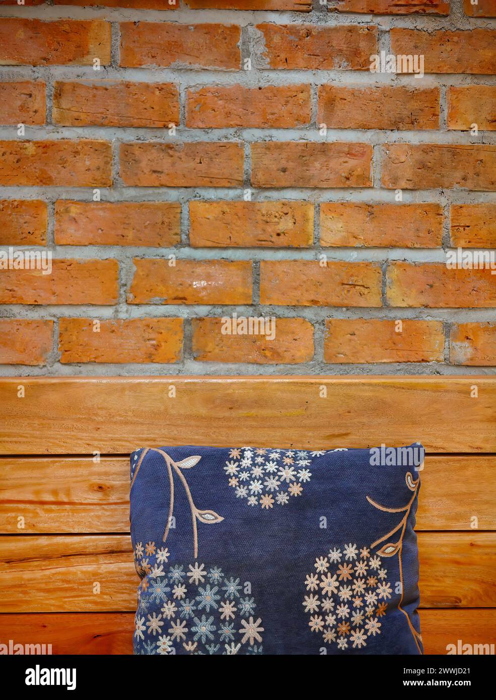 Handgestickte Stoffkissen auf Holzbank mit roter Ziegelwand als Hintergrund, Ruheecke, Kontrastfarben-Design, Wohndekoration Stockfoto