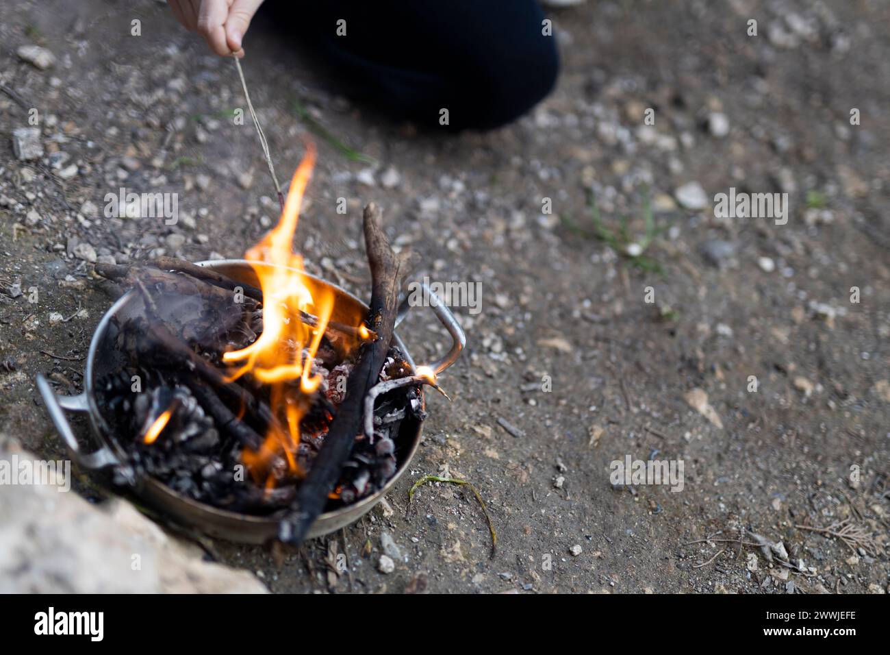 Feuer zündet in einer Blechschale an und die Hand eines Kindes mit einem brennenden Stock Stockfoto