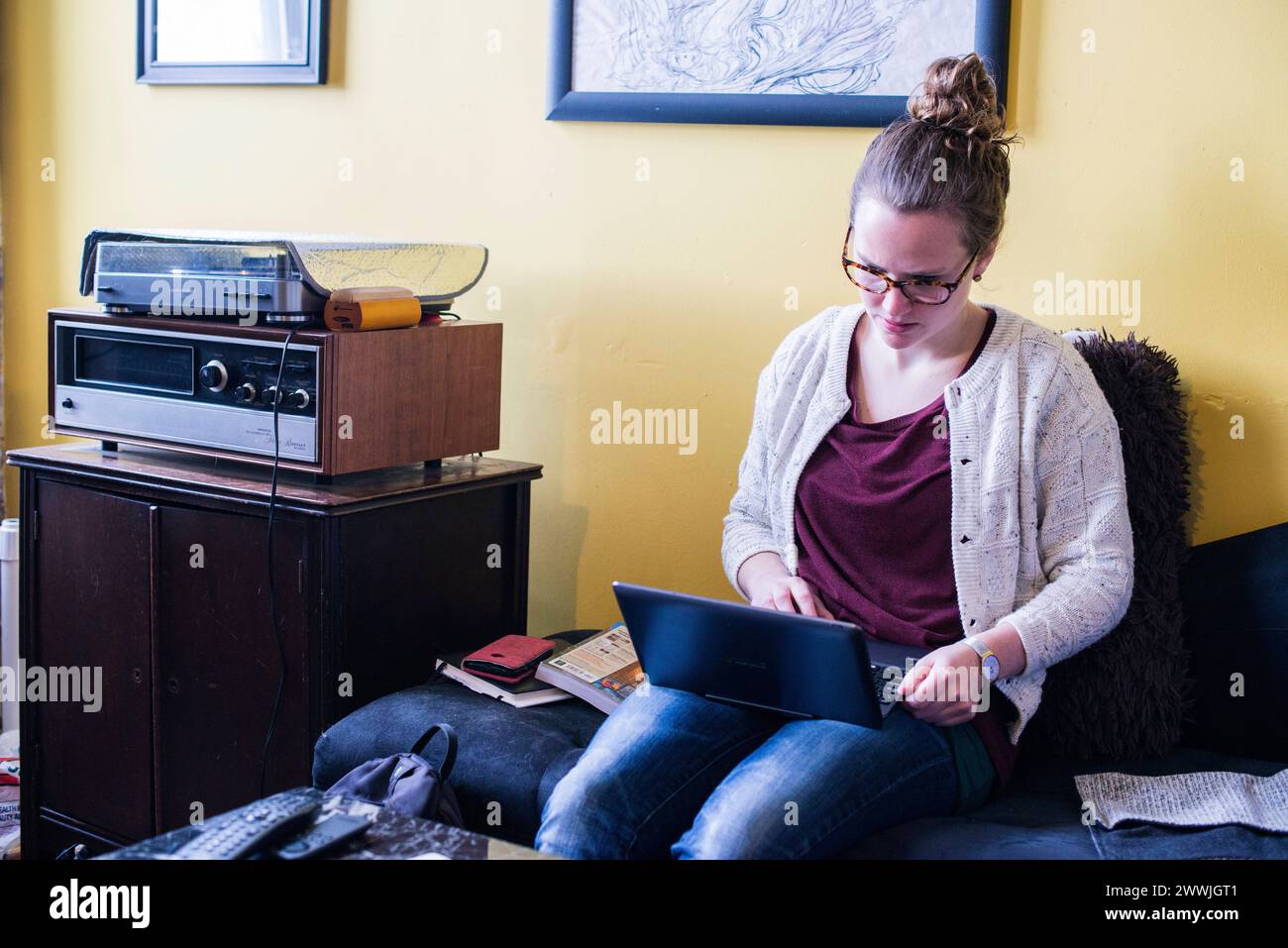 Junge Frau, die an Laptop-Computern arbeitet, New York City, USA. Junge, brünette Frau, die an ihrem Notebook arbeitet, während sie auf einer Bank in ihrem Wohnzimmer sitzt. MRYES New York City 247 Staar Street, Bushwich, Broo New York Vereinigte Staaten von Amerika Copyright: XGuidoxKoppesx Stockfoto