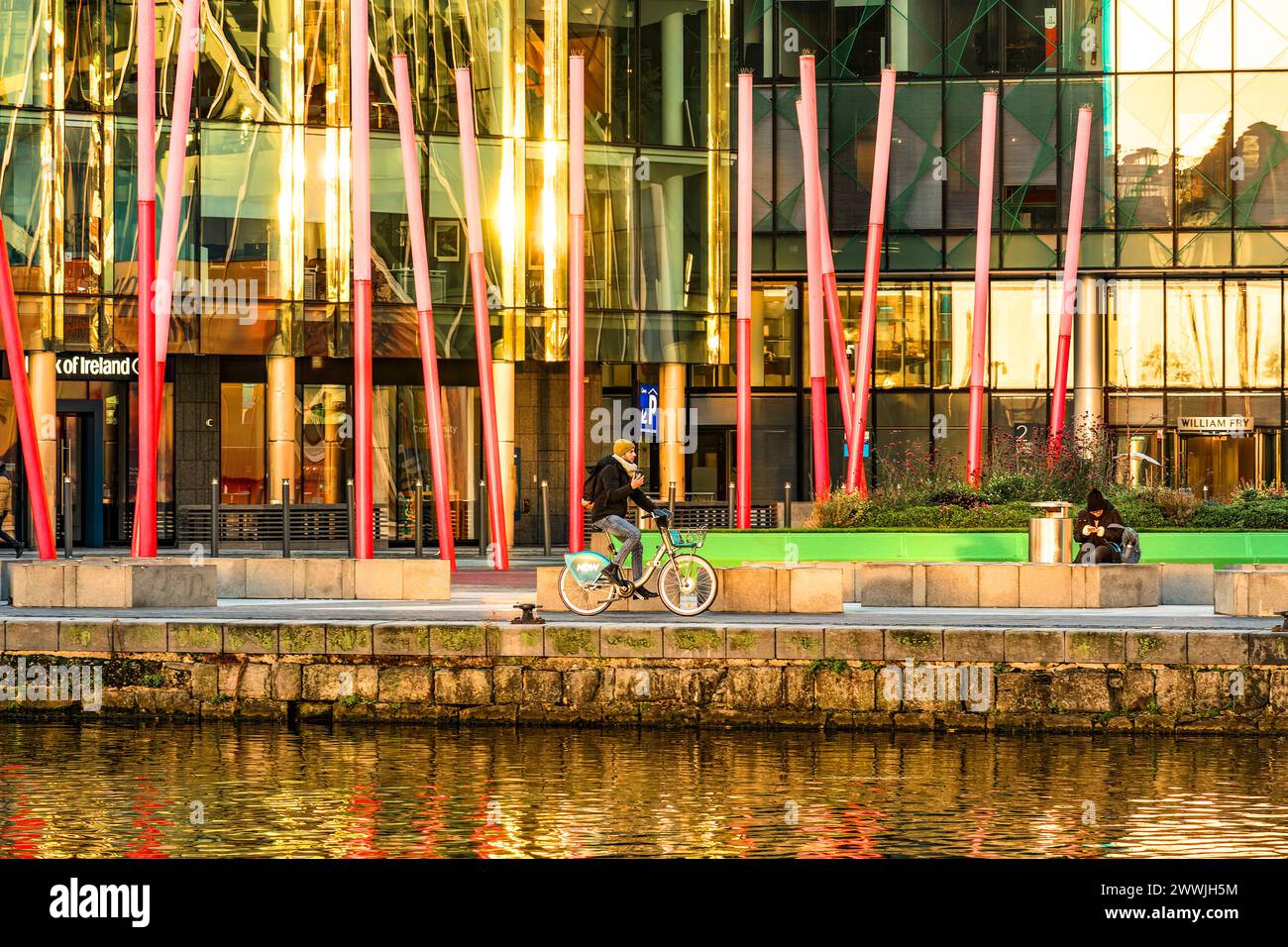 Mann auf einem Stadtrad mit seinem Handy am Grand Canal Dock Plaza vor dem Bord Gáis Energy Theatre. Dublin. Irland. Stockfoto