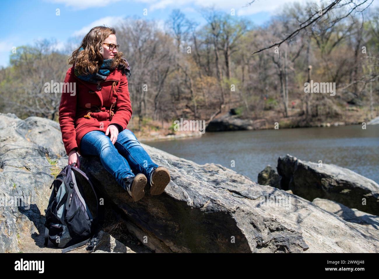 Junge Frau, die den Central Park in New York, USA genießt. Junge Erwachsene, kaukasische Frau mit Blick auf den Teich, die auf einem Felsen sitzt. MRYES New York City Central Park, Manhattan New York Vereinigte Staaten von Amerika Copyright: XGuidoxKoppesx Stockfoto